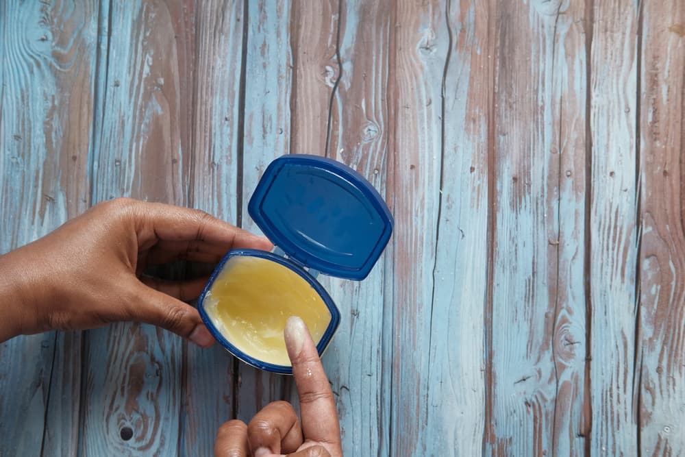 Tub of petroleum jelly and person putting some on finger