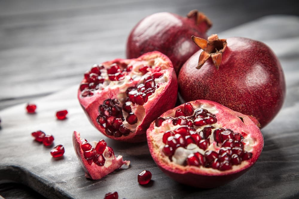Open pomegranates on a table with seeds coming out the flesh