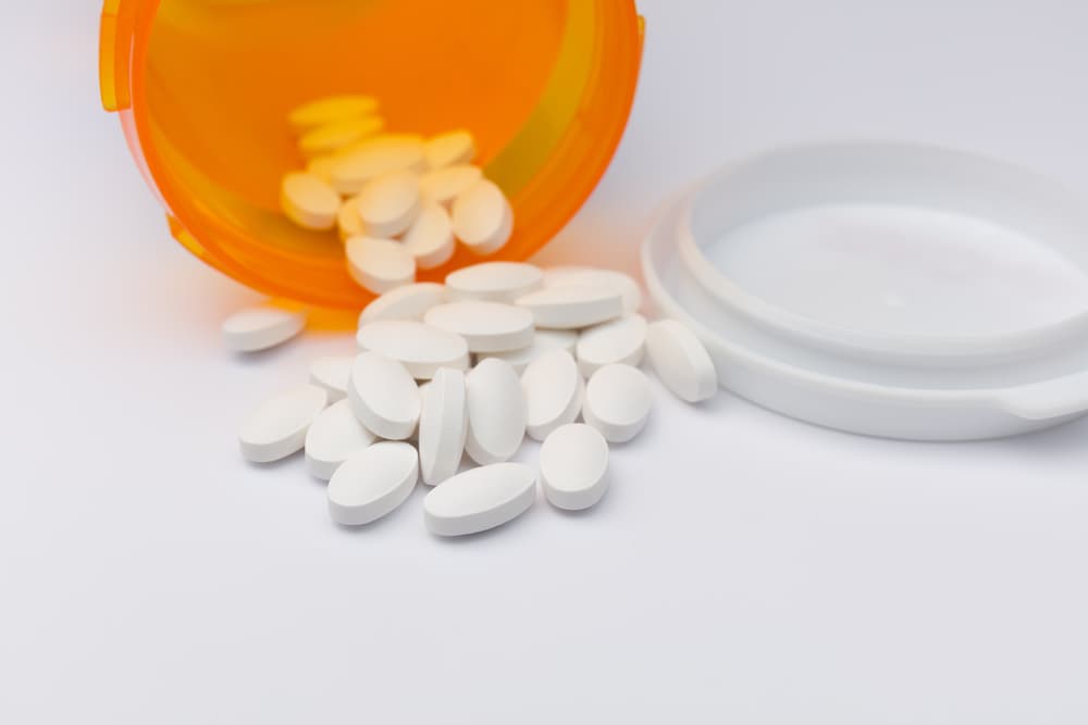 Pill bottle with white small pills falling out of the bottle onto the table