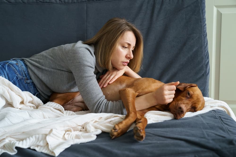 Woman lying down with her dog with blanket
