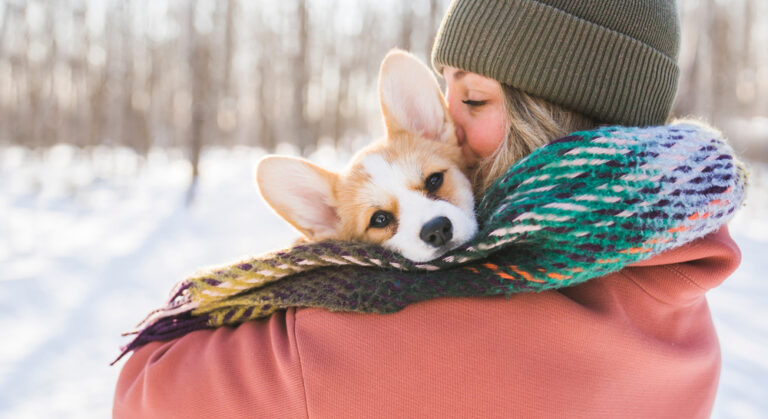 Woman keeping her dog warm in winter amid snowy setting
